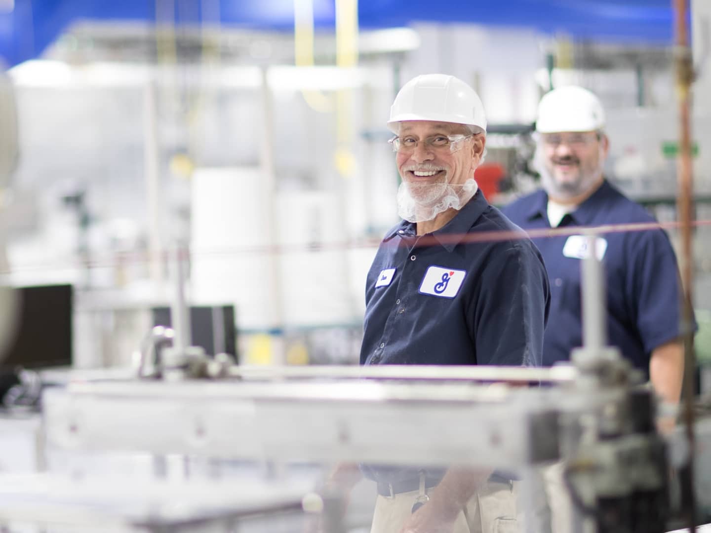 Two manufacturing employees wearing hard hats and smiling